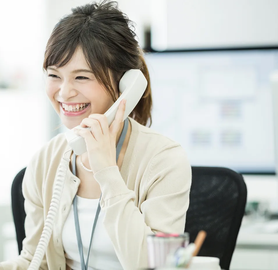 オフィスで電話対応しながら笑顔で対応する女性スタッフ